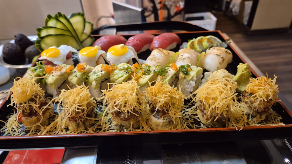 Una fuente de sushi en Hito - nigiri de atún, uramaki de aguacate y rolls con topping crujiente sobre una bandeja de laca